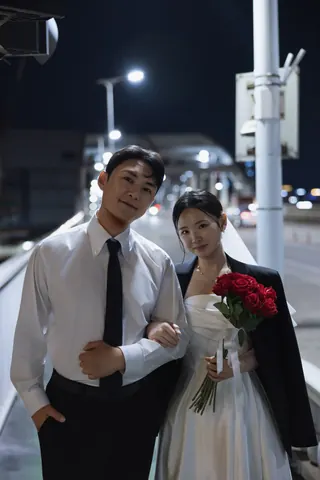 밤거리에서 붉은 장미 꽃다발을 들고 팔짱을 낀 신랑과 신부