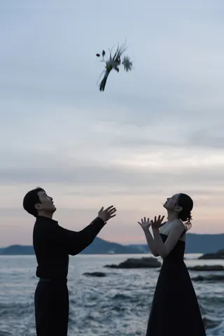 해변 노을 아래 던진 꽃다발을 바라보는 신랑과 신부