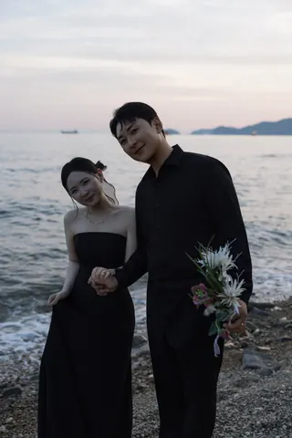 바다를 배경으로 손을 잡고 카메라를 바라보는 신랑과 신부