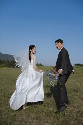 초원에서 꽃다발을 들고 뒤돌아 웃는 신랑과 신부