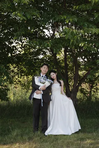 나무 아래에서 꽃다발을 들고 나란히 선 신랑과 신부