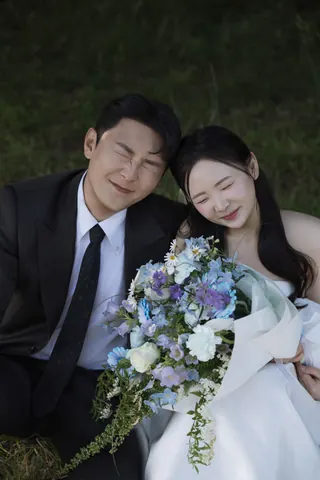 꽃다발을 안고 눈을 꼭 감으며 웃는 신랑과 신부